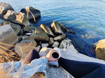 High angle view of woman holding coffee cup on rocks at beach