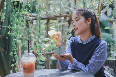 Young woman looking at plant while sitting on seat