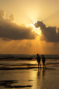 Silhouette men on beach against sky during sunset