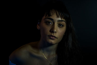 Close-up portrait of young woman against black background