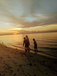 Men on beach against sky during sunset