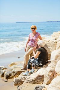 Two elderly women are happy to meet each other, sitting on a rock