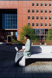 Young businesswoman typing on laptop by office building