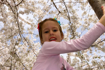 Low angle view portrait of girl on cherry blossom