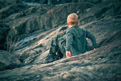 Rear view of boy sitting on rock