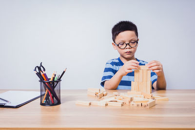 Portrait of young woman playing with toy blocks while sitting on table against white background