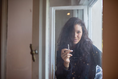 Portrait of woman smoking cigarette by window at home