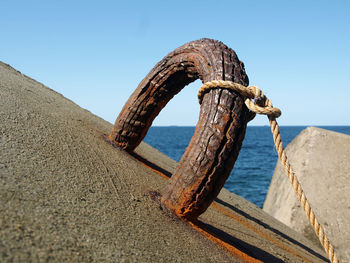 Rusty metallic structure on beach against clear blue sky