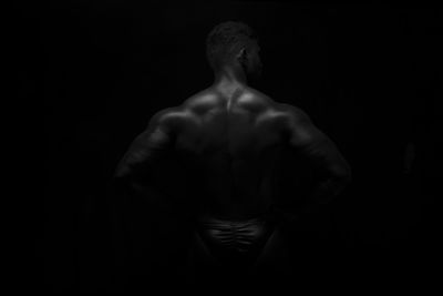 Rear view of shirtless man standing against black background