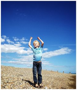 Boy standing on beach against blue sky