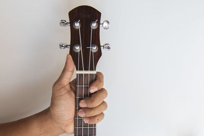 Close-up of hand holding guitar against white background