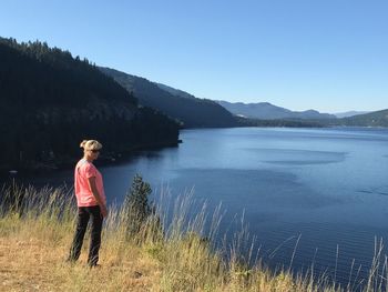 Woman standing by lake against clear blue sky