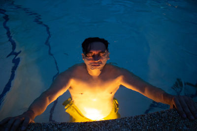 Close-up of man in illuminated swimming pool at dusk