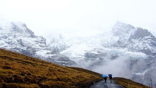 Rear view of people with umbrella walking on mountain during winter