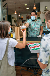 Owner giving pizza take away to customers at restaurant