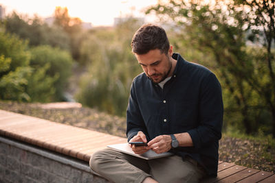 Businessman using smart phone while sitting on bench in park