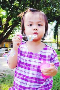 Portrait of cute girl blowing bubble on field