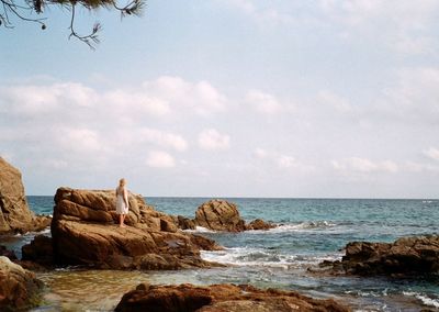 Full length of woman standing on rocks at beach against sky