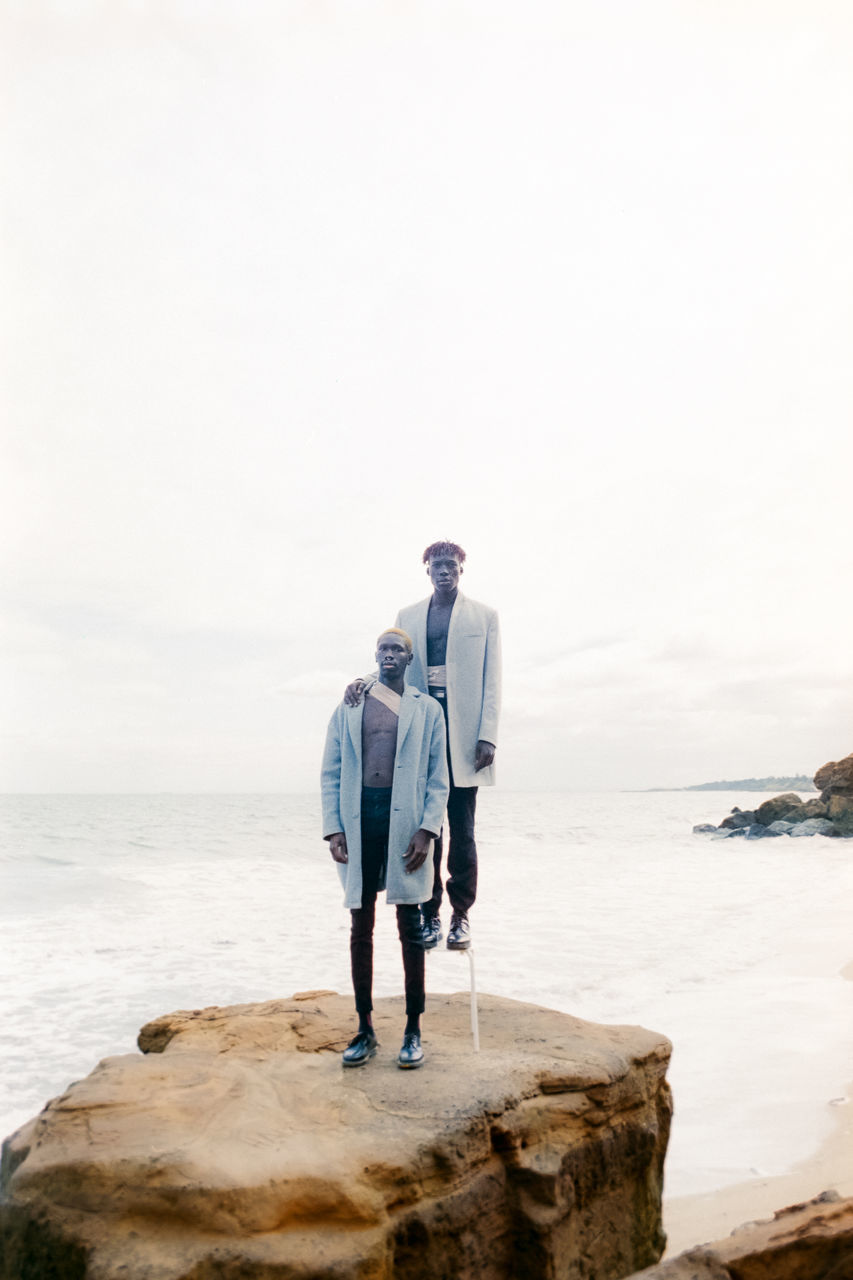 sea, water, full length, sky, standing, rock, rock - object, real people, leisure activity, nature, land, men, copy space, solid, people, scenics - nature, day, beach, beauty in nature, horizon over water, outdoors