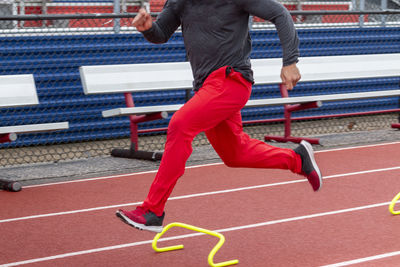 Motion blur on a high school boy running fast over six inch hurdles on a track during practice.