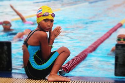 Portrait of girl wearing swimwear sitting at poolside