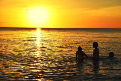 Silhouette people enjoying in sea during sunset