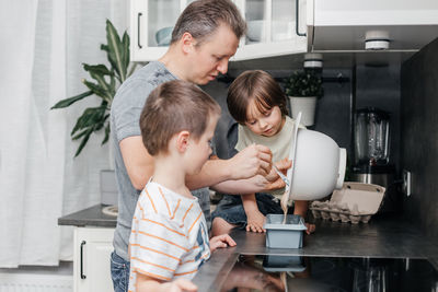 Caring dad is cooking in the kitchen with his two sons. boys and dad prepare pie dough