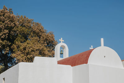 Whitewash church with red dome on a hill in mykonos, greece, against blue sky.