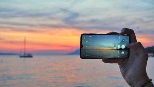 Woman photographing sea against sky during sunset