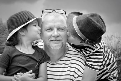 Grandchildren kissing grandfather against sky