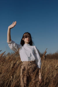 Young woman in white blouse standing in field of dry pampas grass in front of sky covering face