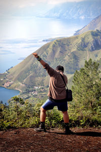 Rear view of man standing on mountain against sky