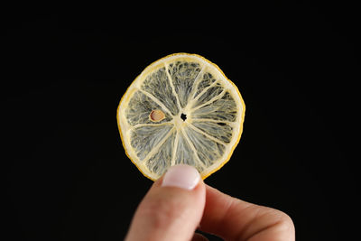 Close-up of hand holding lemon against black background