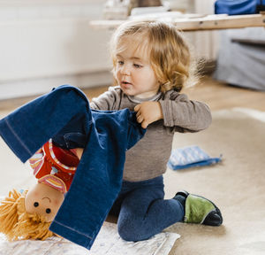 Cute girl holding jeans while sitting on floor at home