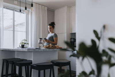 Pregnant woman using phone while making coffee