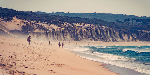 People walking on beach against clear sky