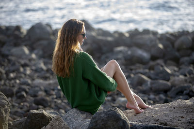 Beautiful woman sitting on rock at beach