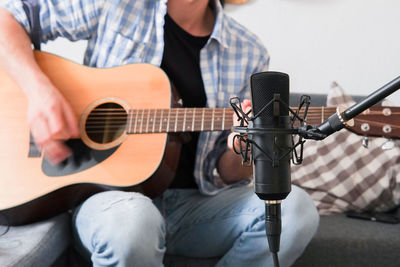 Midsection of man playing guitar with microphone in foreground