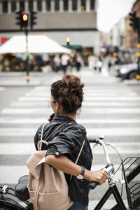 Woman with bicycle standing on zebra crossing in city