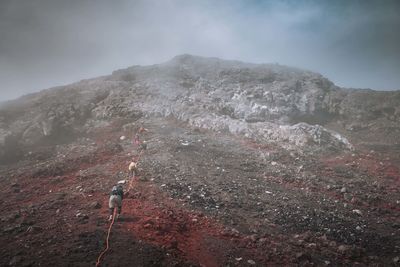 Low angle view of hikers climbing mountain against sky