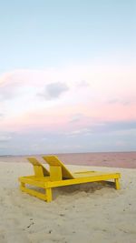 Yellow lounge chairs on sea shore against sky during sunset