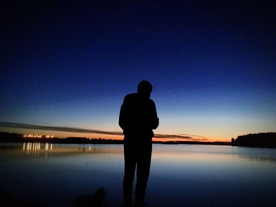 SILHOUETTE MAN STANDING ON LAKE AGAINST SKY AT SUNSET