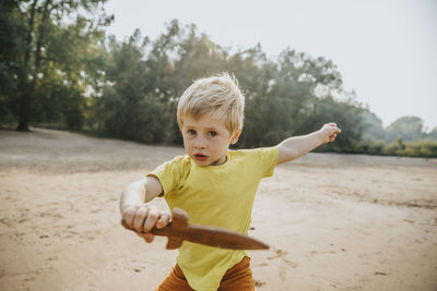 Cute little boy playing with wooden dagger at beach