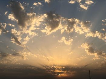 Low angle view of sunlight streaming through clouds during sunset