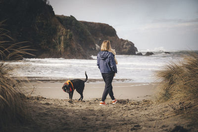 A woman with an infant is playing with a dog on the californian beach