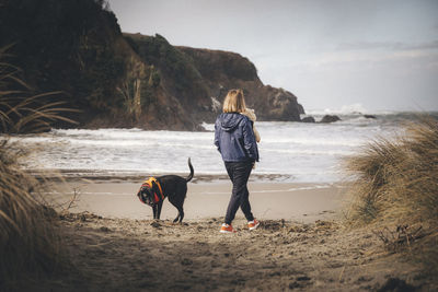 Friends walking on shore at beach against sky