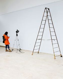 Woman with tripod and ladder standing against wall