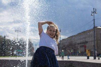 Happy little cute girl having fun in splashes a fountain