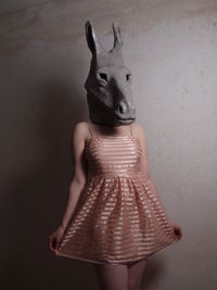 Woman wearing animal mask while standing against wall