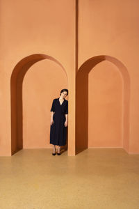 Trapped young woman leaning on arch over orange wall